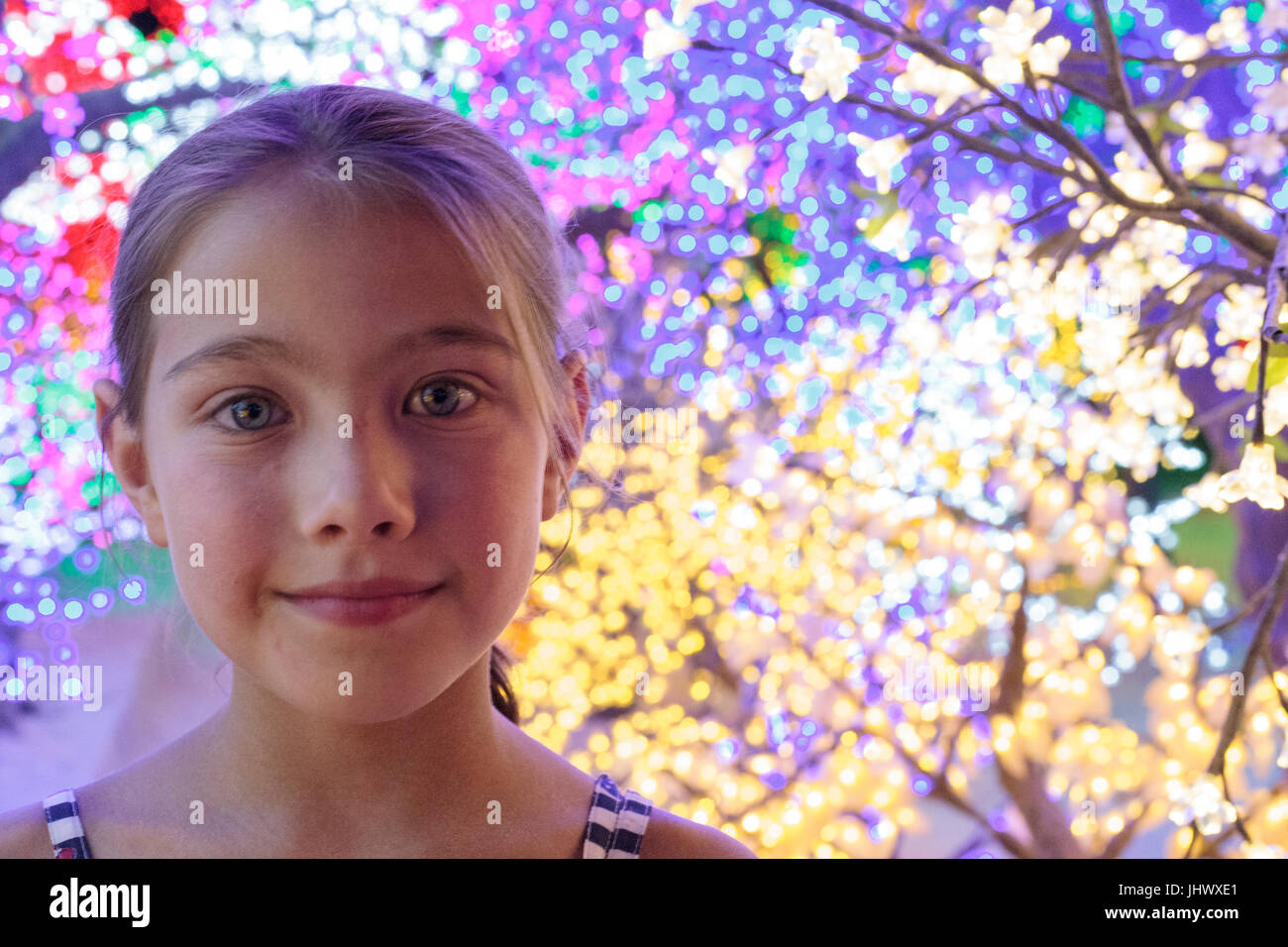 Sorridente giovane ragazza caucasica con luci luminose in tress dietro di lei Foto Stock
