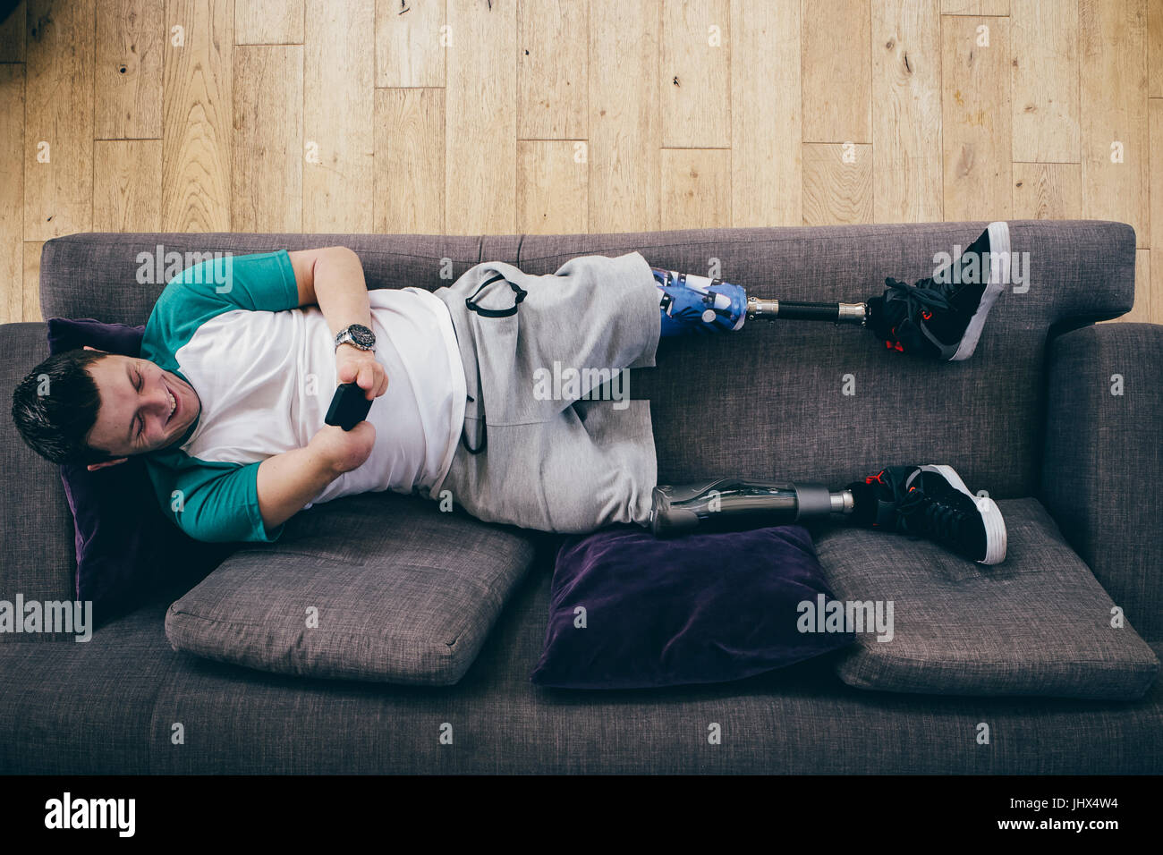 Quadriplegic Uomo sdraiato sul divano di casa. Egli sta usando uno smartphone. Foto Stock