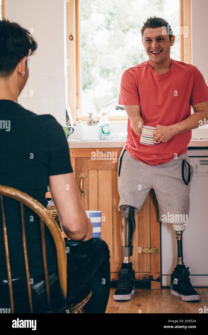 Quadriplegic man standing nella sua cucina. Egli è di avere una conversazione con il suo amico ed entrambi sono bere il tè. Foto Stock
