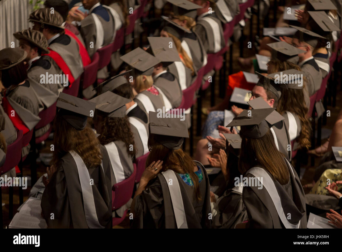 Giovani laureati che indossa abiti noleggiati e mortarboards sedersi nella sala centrale della loro università, attesa per la loro cerimonia di laurea per iniziare, il 13 luglio 2017, presso l'Università di York, Inghilterra. Foto Stock