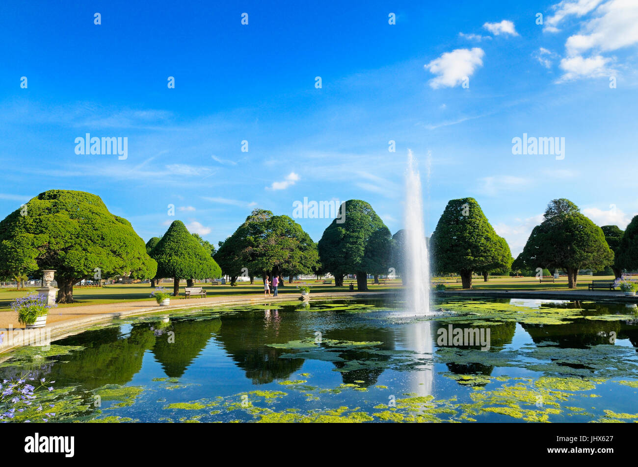 Un paio di prendere una passeggiata intorno alla grande fontana giardino circondato da antichi alberi di tasso su un perfetto pomeriggio d'estate, Hampton Court Palace Gardens Foto Stock