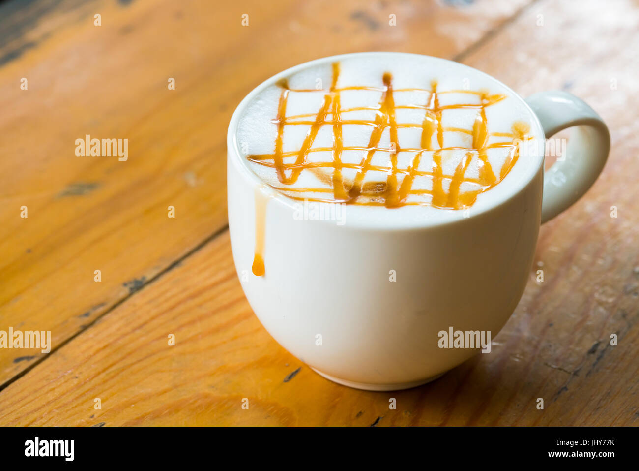 A caldo il caffè macchiato con caramello in tazza bianca sulla tavola di legno dalla luce della finestra Foto Stock