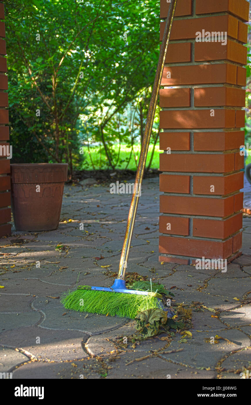 Una scopa verde con maniglia arrugginita appoggiarsi al pilastro di mattoni Foto Stock
