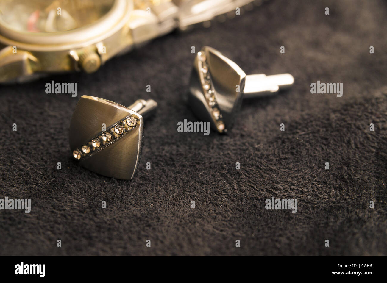 Gemelli in argento con cristalli giacere uno dopo l'altro su un panno nero accanto a un orologio dorato Foto Stock