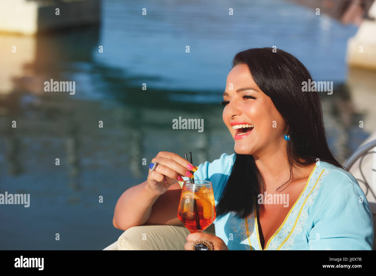 Felice di abbronzatura bella donna seduta e bevendo cocktail in Seaside Cafe, il fuoco selettivo Foto Stock