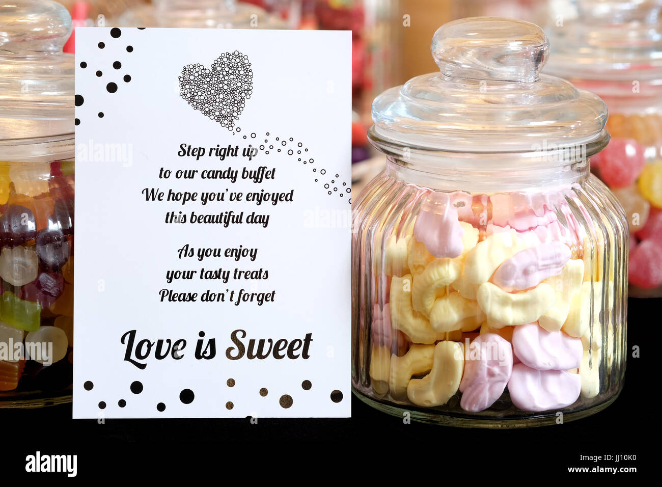 Un vasetto di vetro vecchio stile di dolci di schiuma gialli e rosa lasciato su un tavolo, con altre prelibatezze dolci, come buffet dolce o caramella in un ricevimento di nozze Foto Stock
