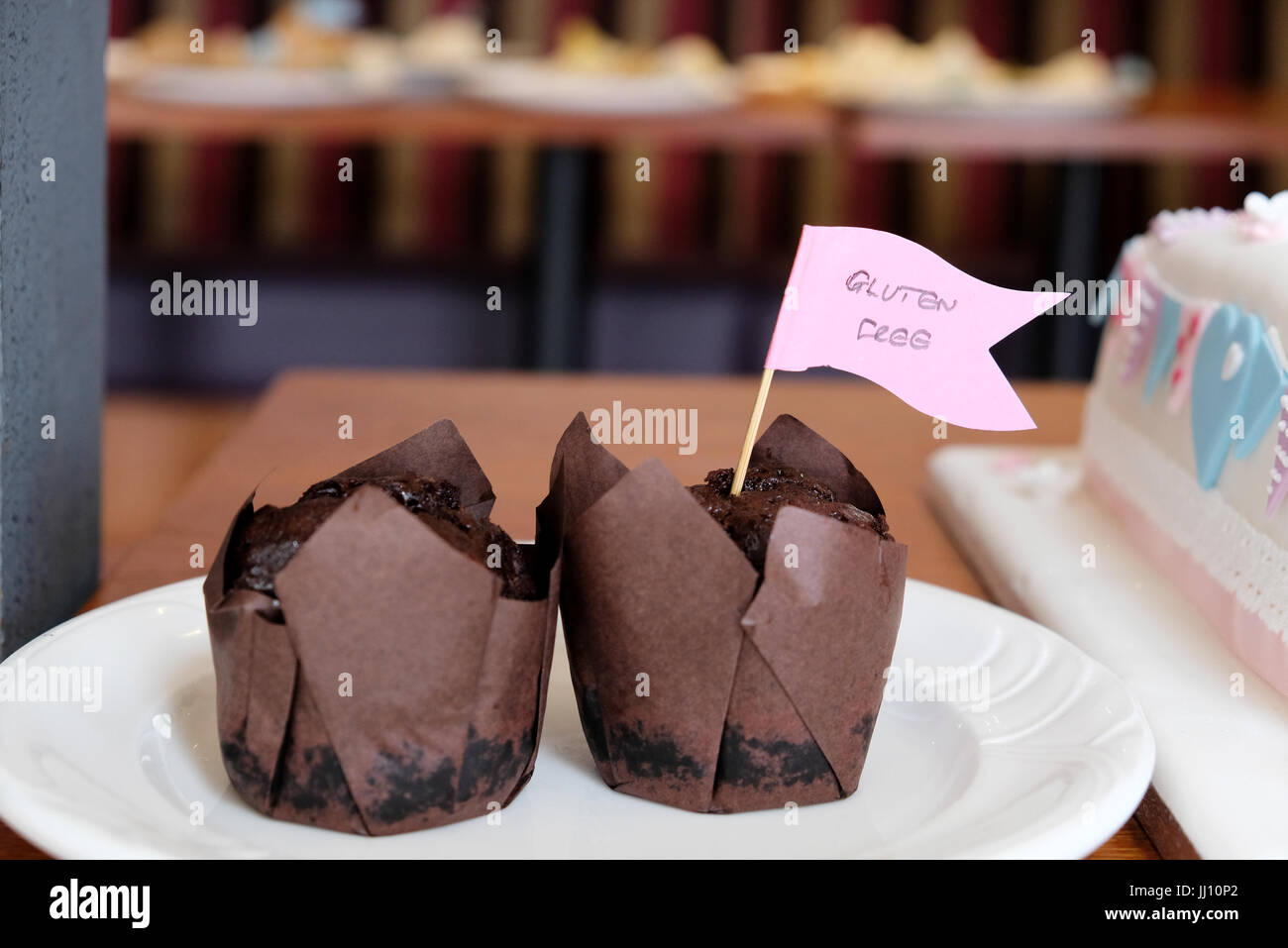 Due tortine di muffin al cioccolato, avvolte in casse di carta marrone, contrassegnate con una bandiera come prive di glutine, su un piatto come parte di un buffet di tavola Foto Stock