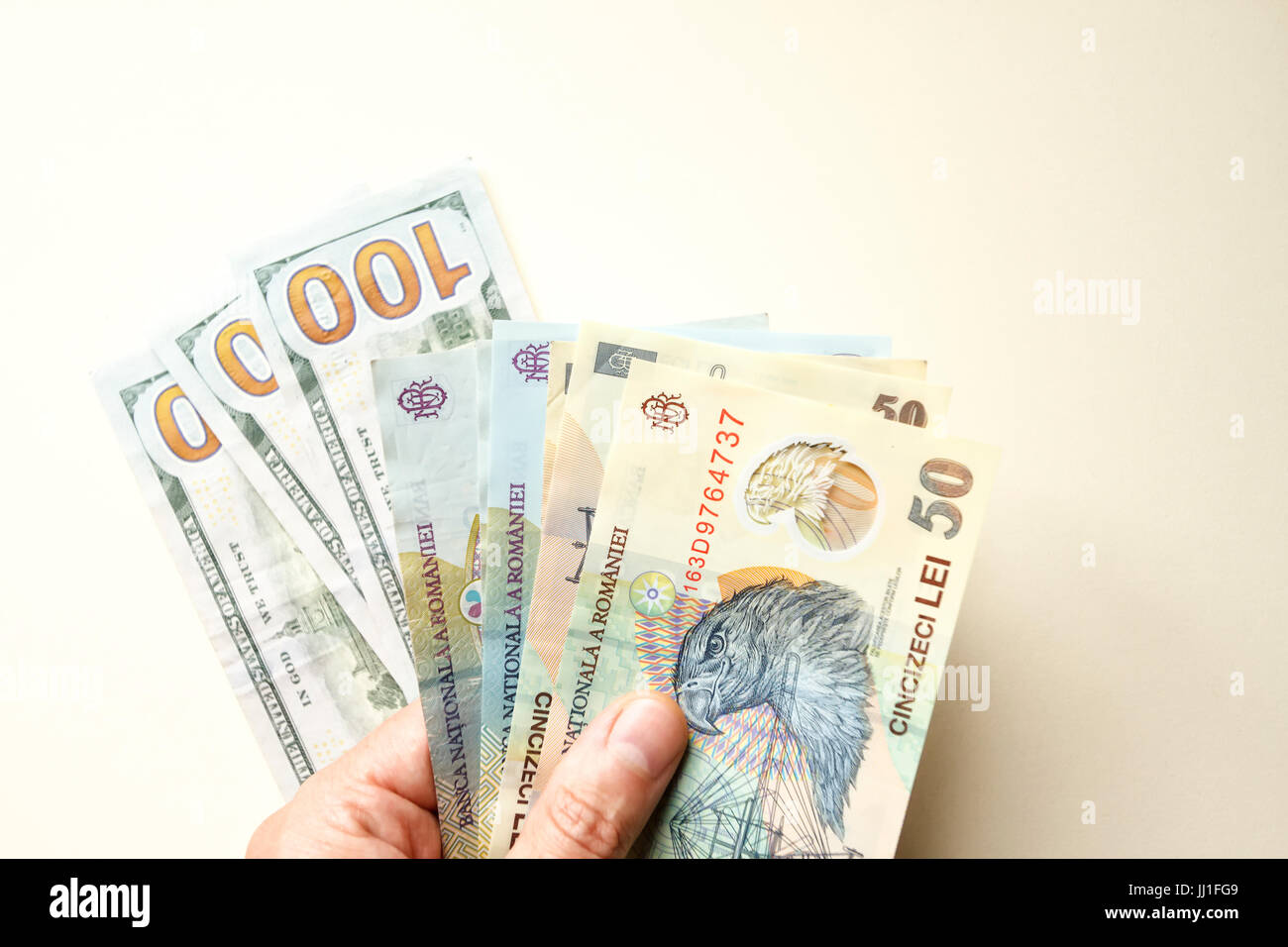 Mano che tiene in mano dollari USA e banconote rumene lei (USD e RON) – concetto di finanza, risparmio, investimento e denaro. Foto Stock