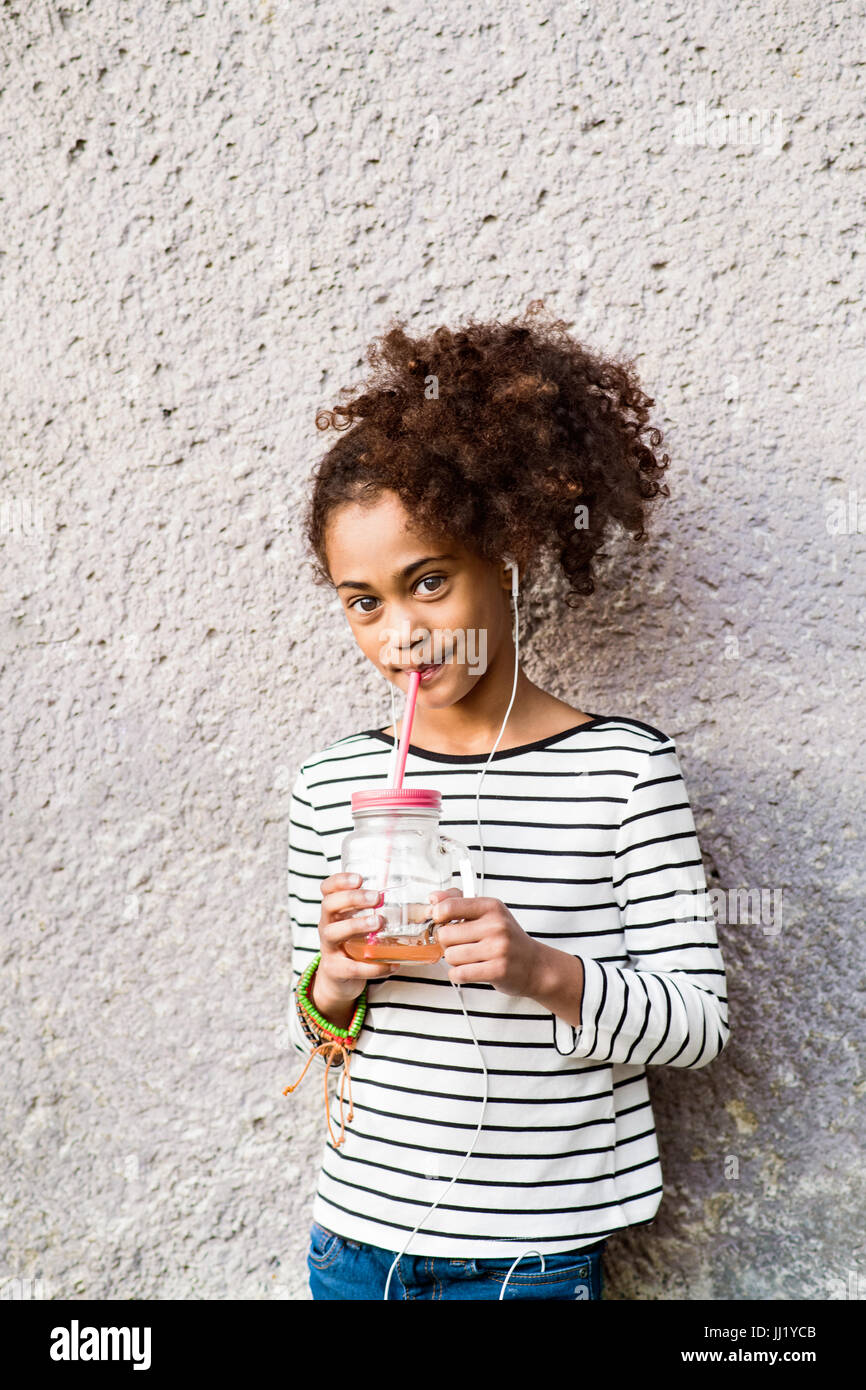 Bella African American Girl di bere succo di frutta, ascoltando musica. Foto Stock