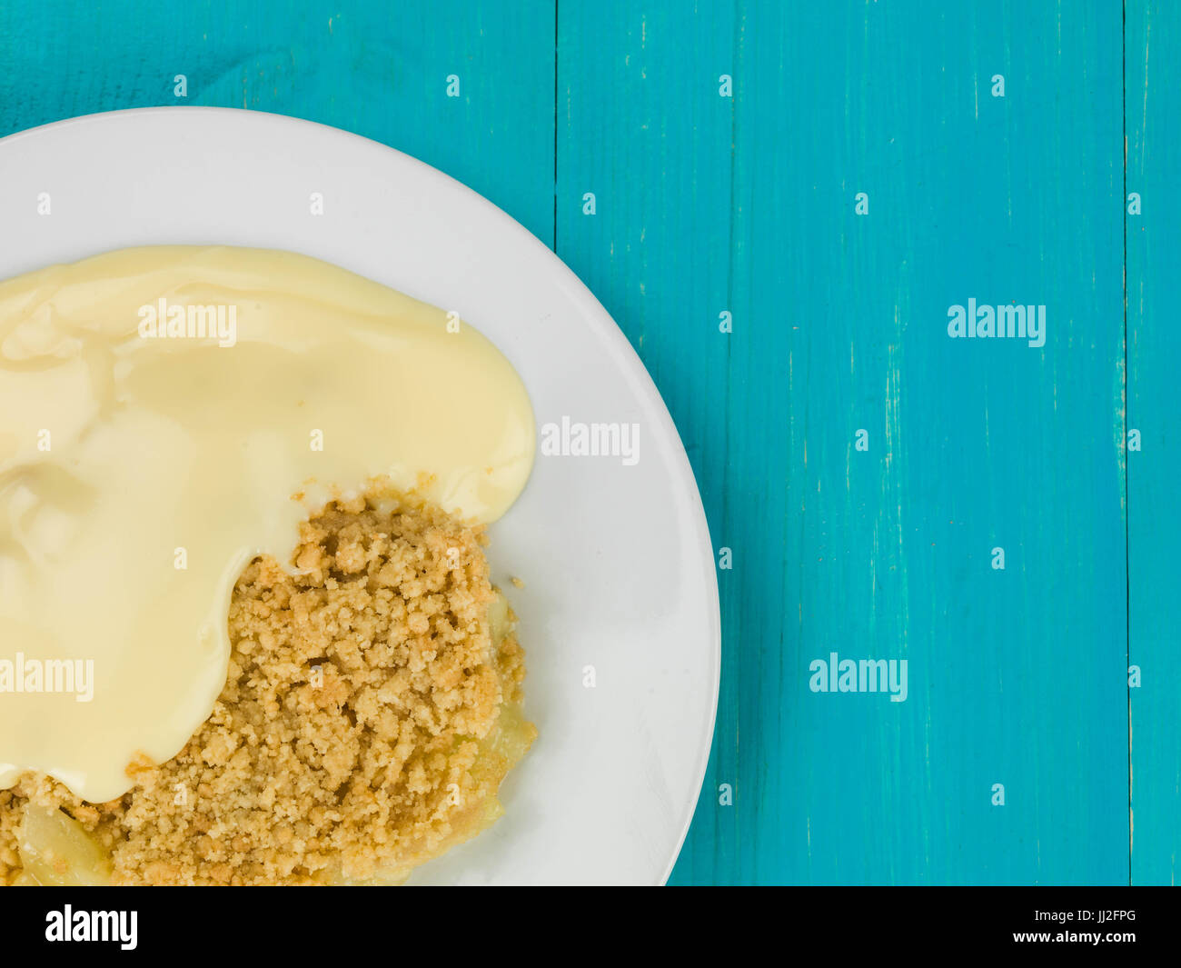 Apple Crumble dessert servito con crema pasticcera calda contro un blu sullo sfondo di legno Foto Stock