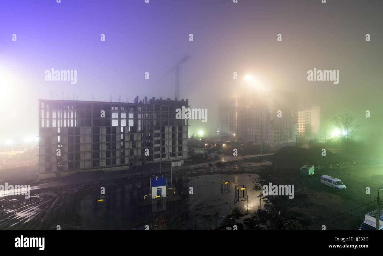 Forte nebbia durante la notte in un cantiere con lo scheletro di un alto edificio in costruzione Foto Stock