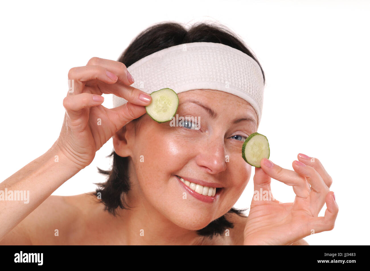 Allegra donna matura tenendo i pezzi di cetriolo davanti agli occhi. Natural spa trattamento. Isolato su sfondo bianco Foto Stock
