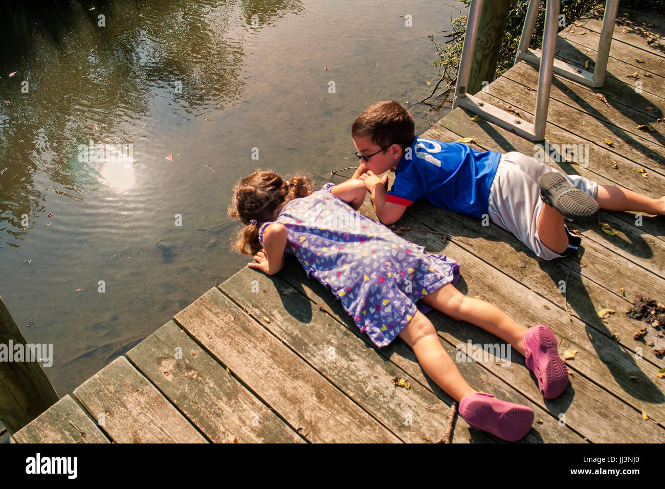 6-7 anno vecchia ragazza e Ragazzo che guarda oltre il bordo del dock - guardando il pesce. estate scenic Foto Stock