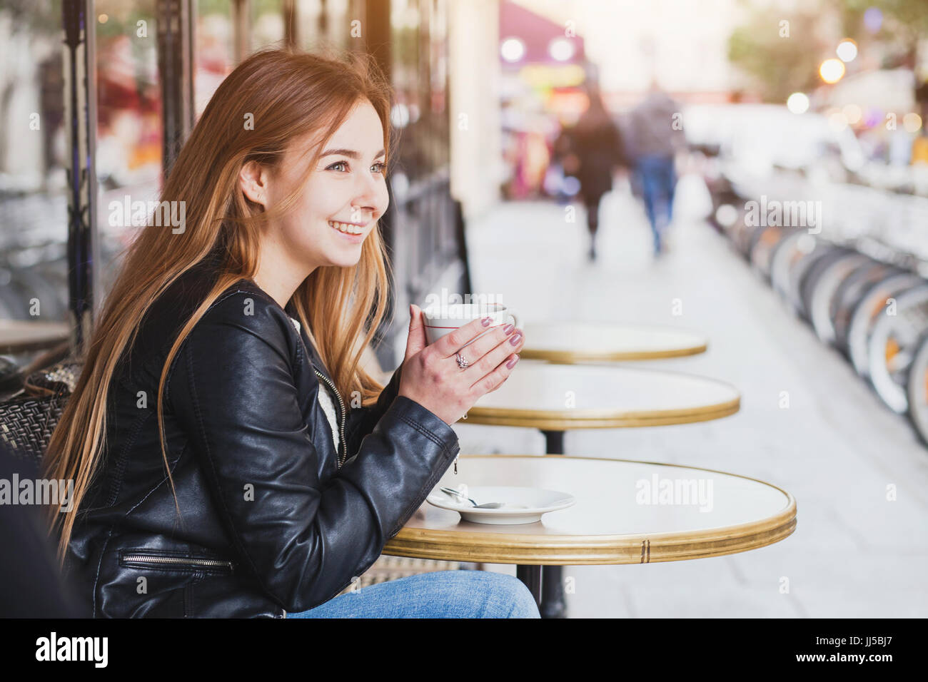 Sorridenti attraente giovane donna con tazza di caffè nella caffetteria di strada in Europa, bella ragazza a Parigi Foto Stock