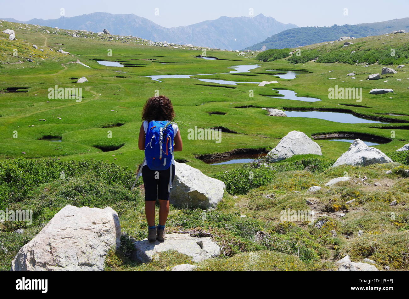 Escursionista femmina (giovane adulto) sull'altopiano bagnato I Pozzi, coperto con piccoli laghi e campi verdi. Foto Stock