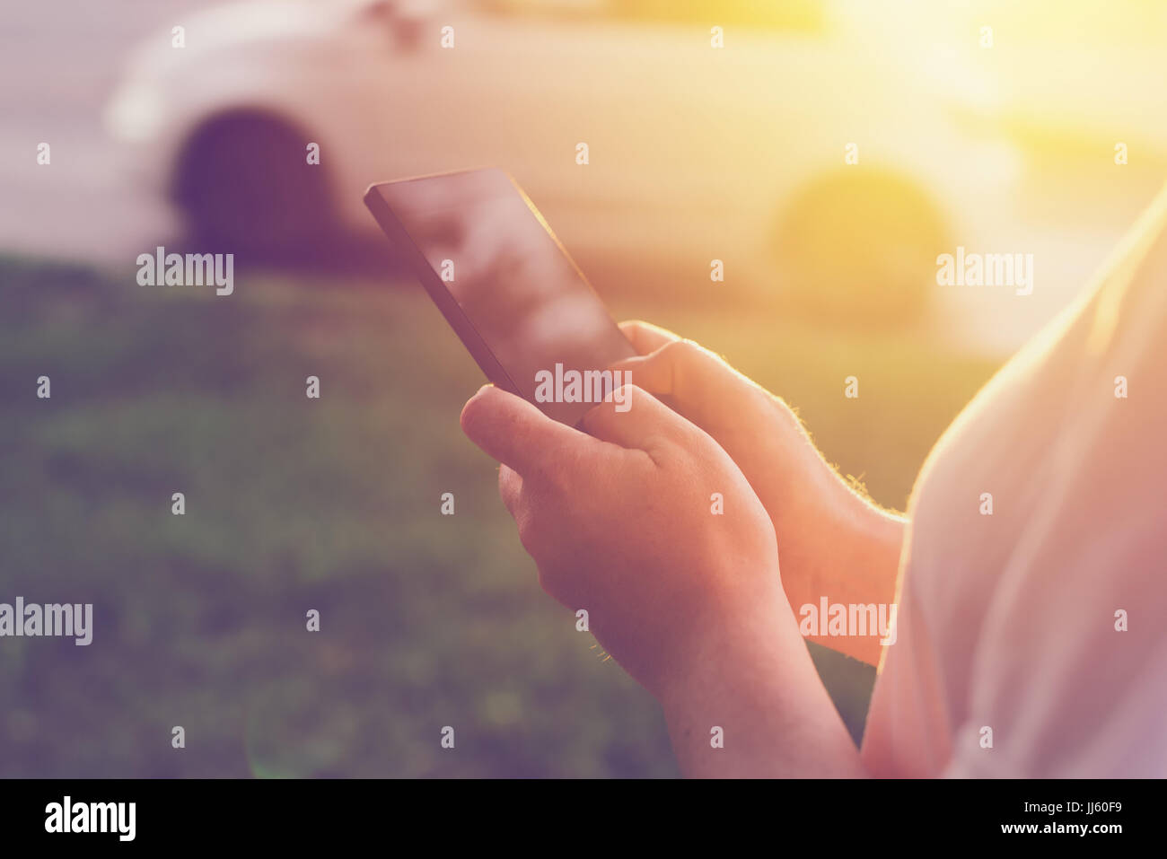 Donna che utilizza il telefono mobile app per chiamare un taxi sulla strada a tramonto Foto Stock