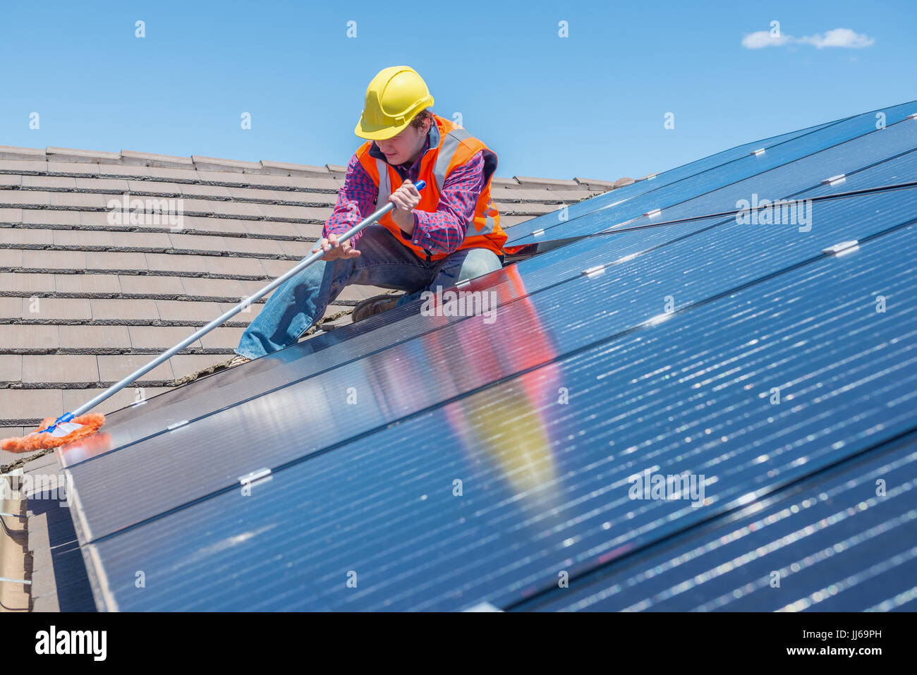 Giovane lavoratore la pulizia di pannelli solari sul tetto della casa Foto Stock