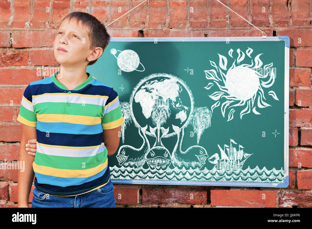 Ragazzo meditativo nei pressi di lavagna con disegno mappa terrestre su tre balene nell'improvvisata classe esterna Foto Stock