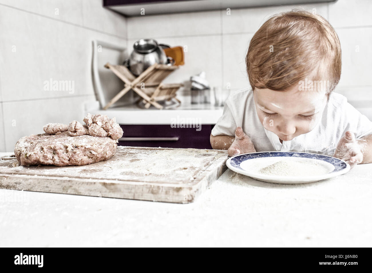 Baby boy preparando polpette di carne. Lui sta cercando il piatto pieno di pane grattugiato Foto Stock