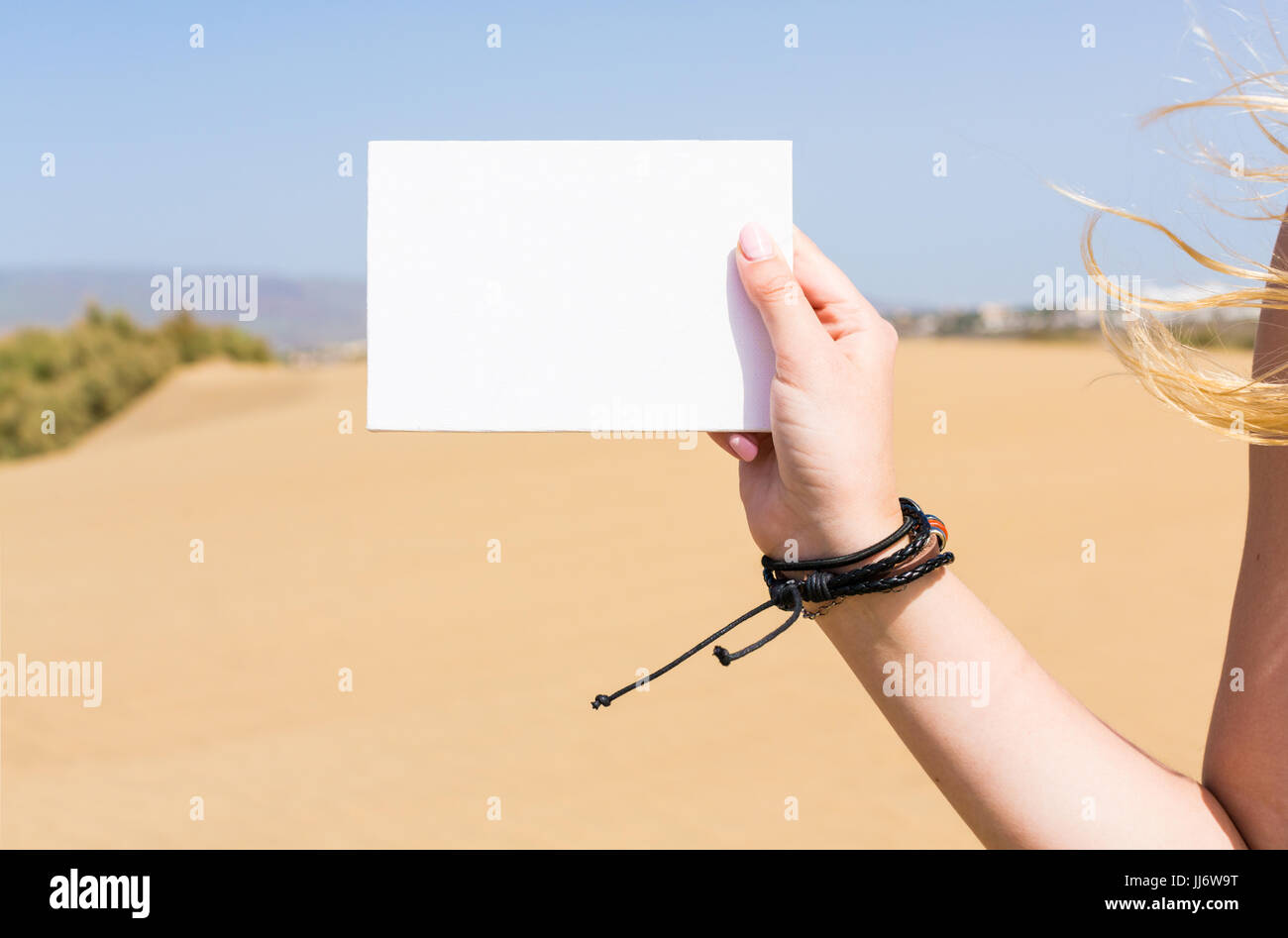 Cartolina di vuoto in una mano della ragazza contro un deserto sabbioso sfondo Foto Stock