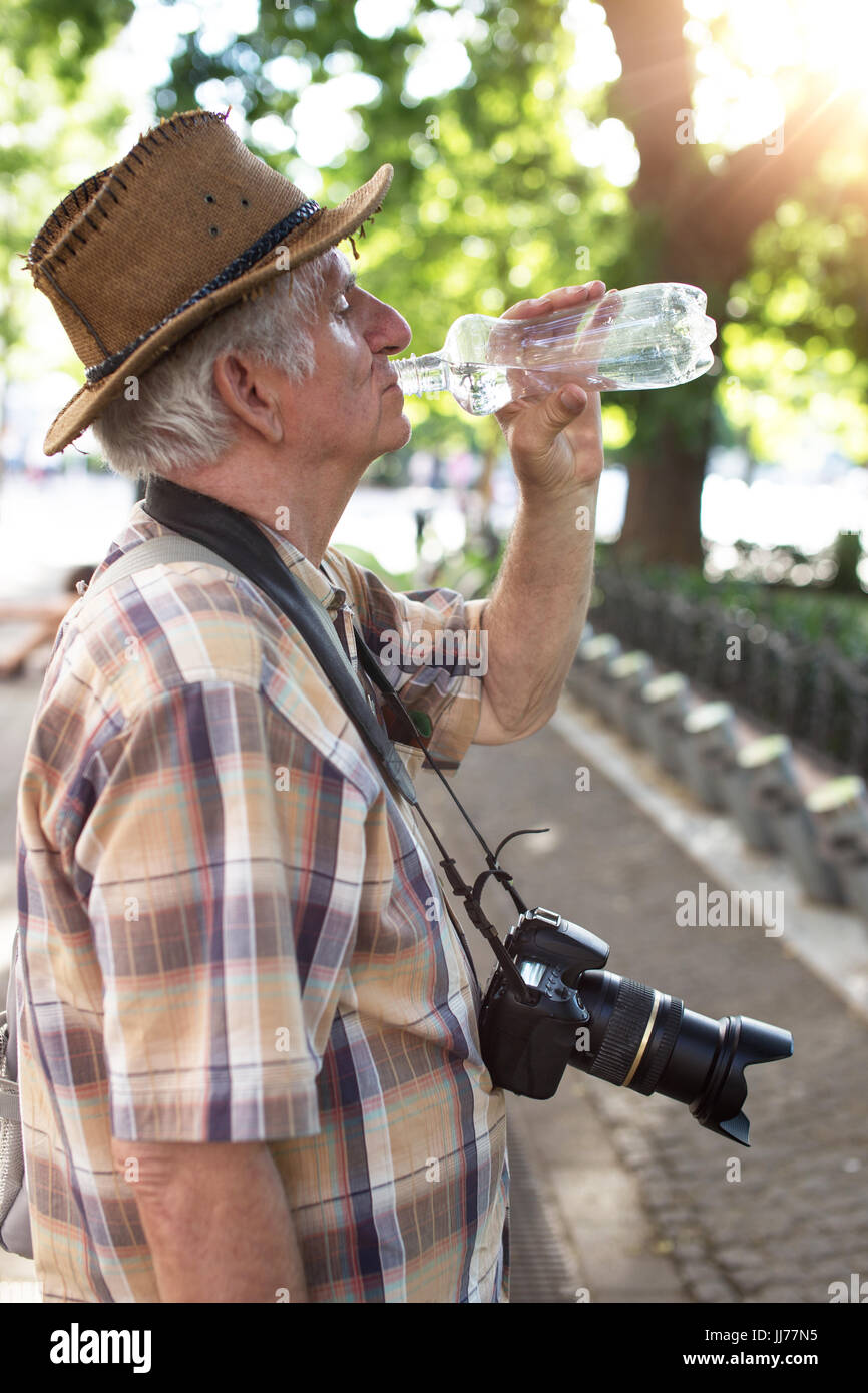 Anziano pensionato tourist uomo acqua potabile dalla bottiglia in posizione di parcheggio Foto Stock
