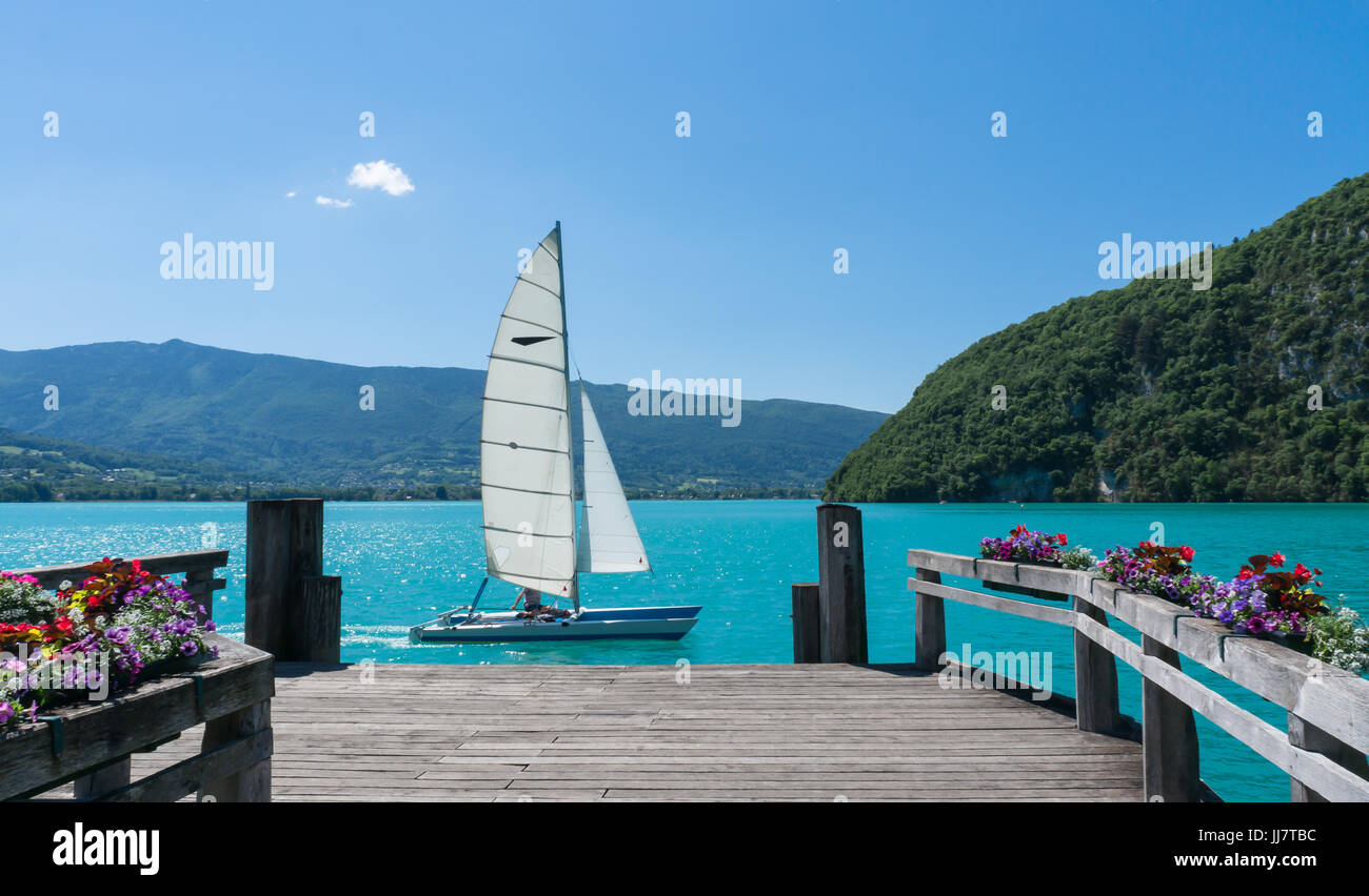 Un bel bianco in barca a vela è passato un dock in legno su Lac d'Annecy nel sud della Francia. Foto Stock