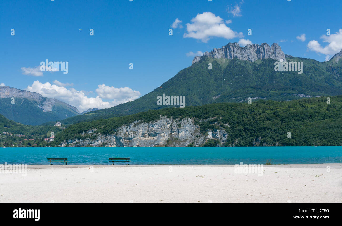 Sui banchi di sabbia bianca nella parte anteriore delle acque turchesi del Lac d'Annecy nel sud della Francia, bella montagna in background. Foto Stock