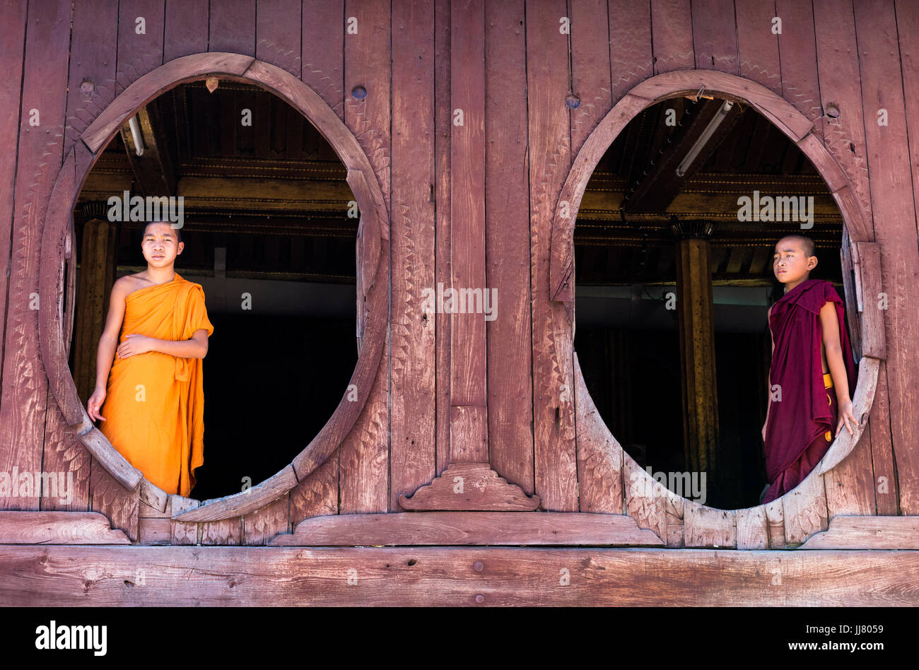 Due monaci novizio nelle finestre ovali del legno di shwe yaunghwe kyaung monastero, nyaung shwe, stato shan, myanmar Foto Stock