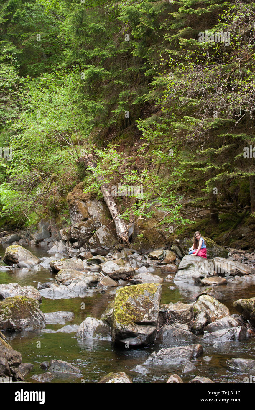 Ragazza sulle rocce accanto al fiume vicino a Plodda Falls, Allt na Bodachan, Inverness-shire, Scozia, Isole britanniche Foto Stock