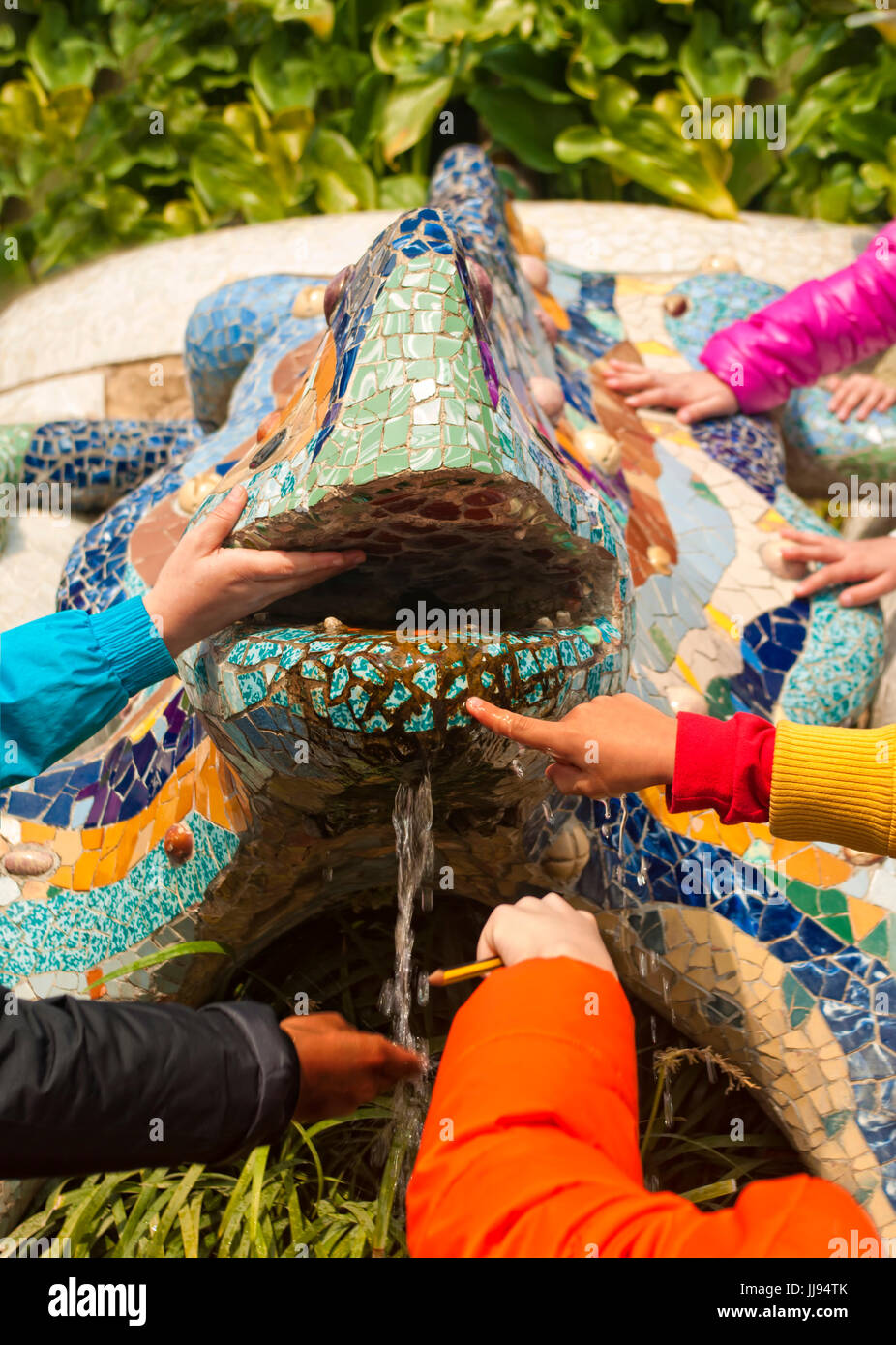 Multi-etnico bambini di scuola elementare di mani toccano famoso Antonio Gaudi drago mosaico Fontana nel parco Guell su un campo scuola-viaggio in Barcelo Foto Stock