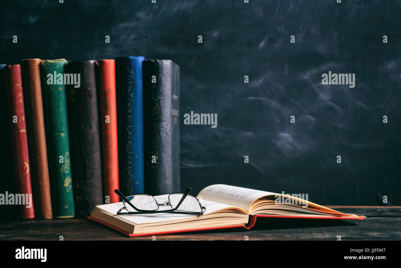 Il concetto di istruzione. Libri antichi e occhiali su sfondo blackboard Foto Stock