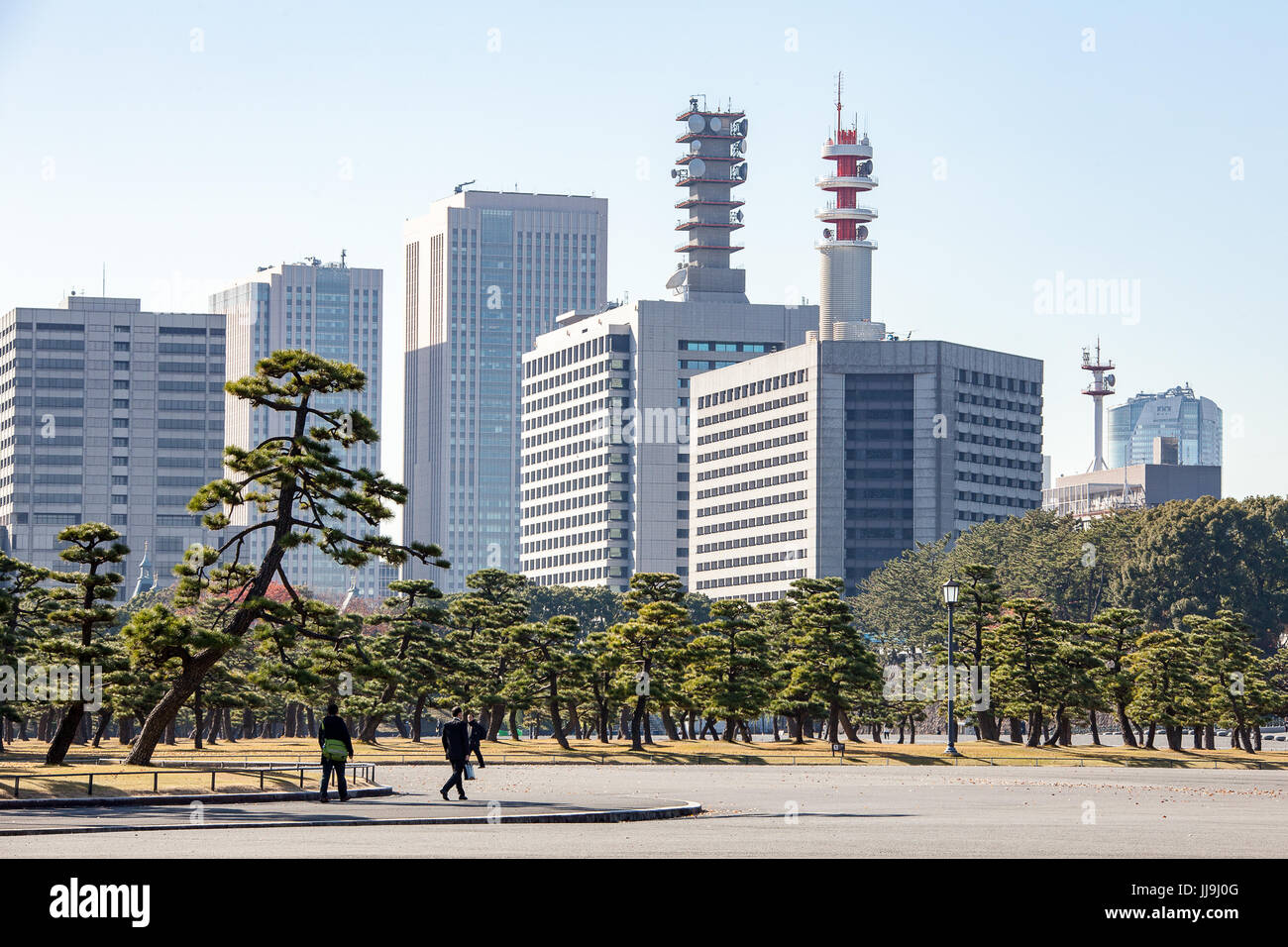 La gente a piedi attraverso un parco di pini su uchibori dori road, Tokyo con il dipartimento di polizia e altri edifici del governo in background Foto Stock