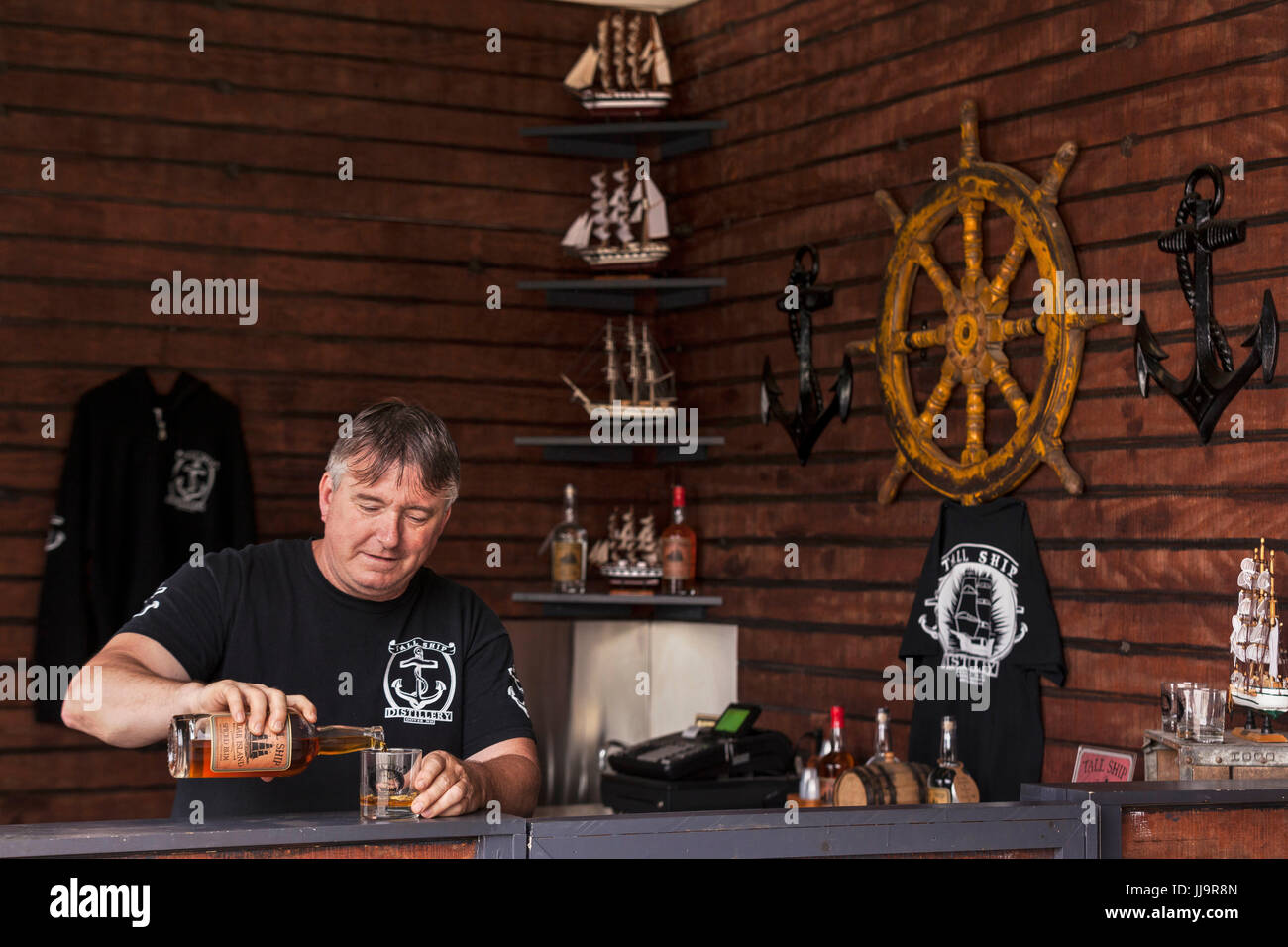 Il distillatore versa un campione di vetro spiced rum nel suo negozio vetrine. Foto Stock