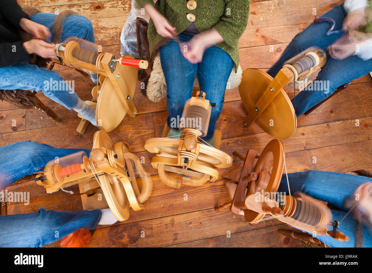 Fotografato dal di sopra, un cerchio di donne gira lana in filato utilizzando il pedale azionato da ruote di filatura. Foto Stock