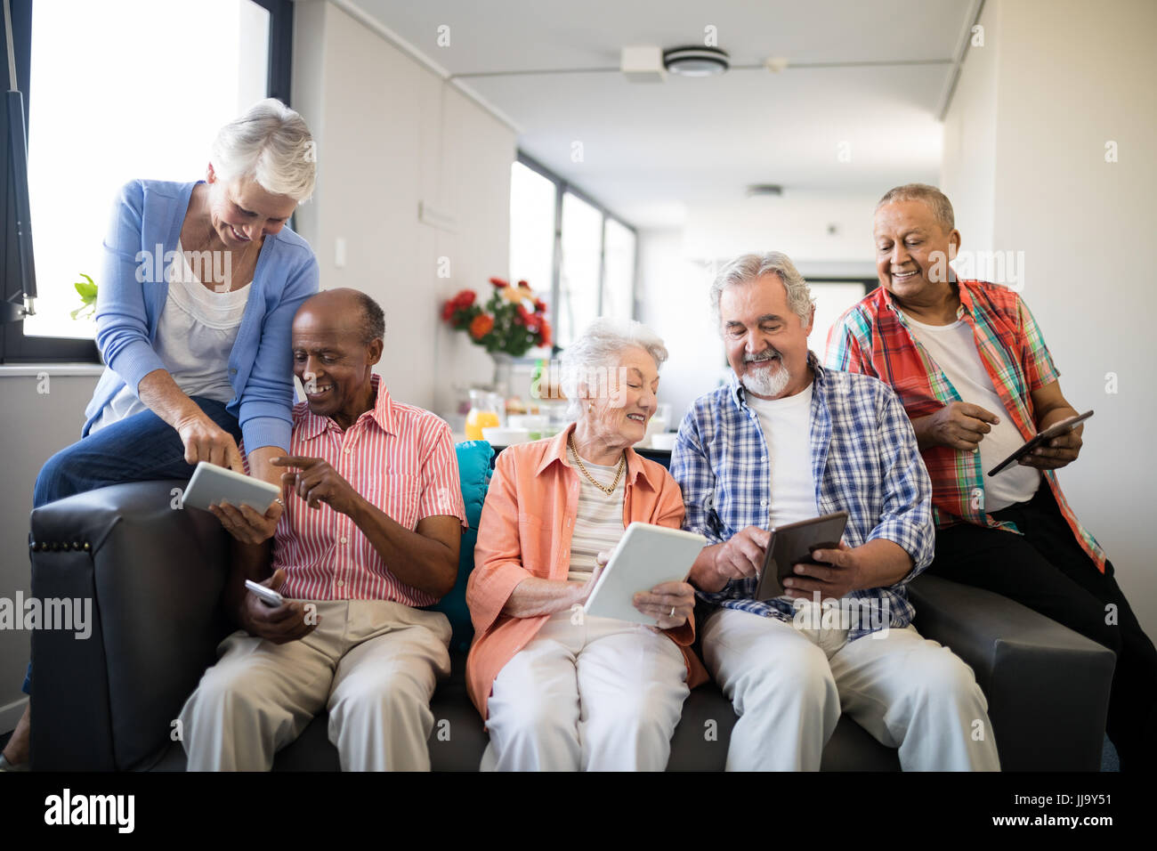 Senior felici le persone che usano i computer tablet comodamente seduti sul divano di casa di cura Foto Stock