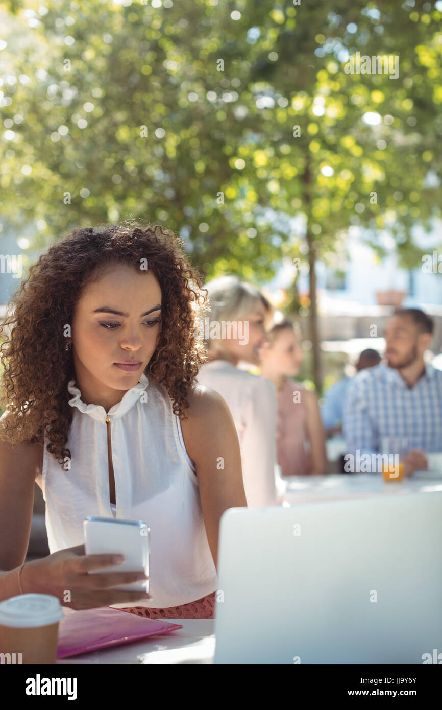 Bella donna utilizzando il telefono cellulare e il computer portatile in ristorante Foto Stock