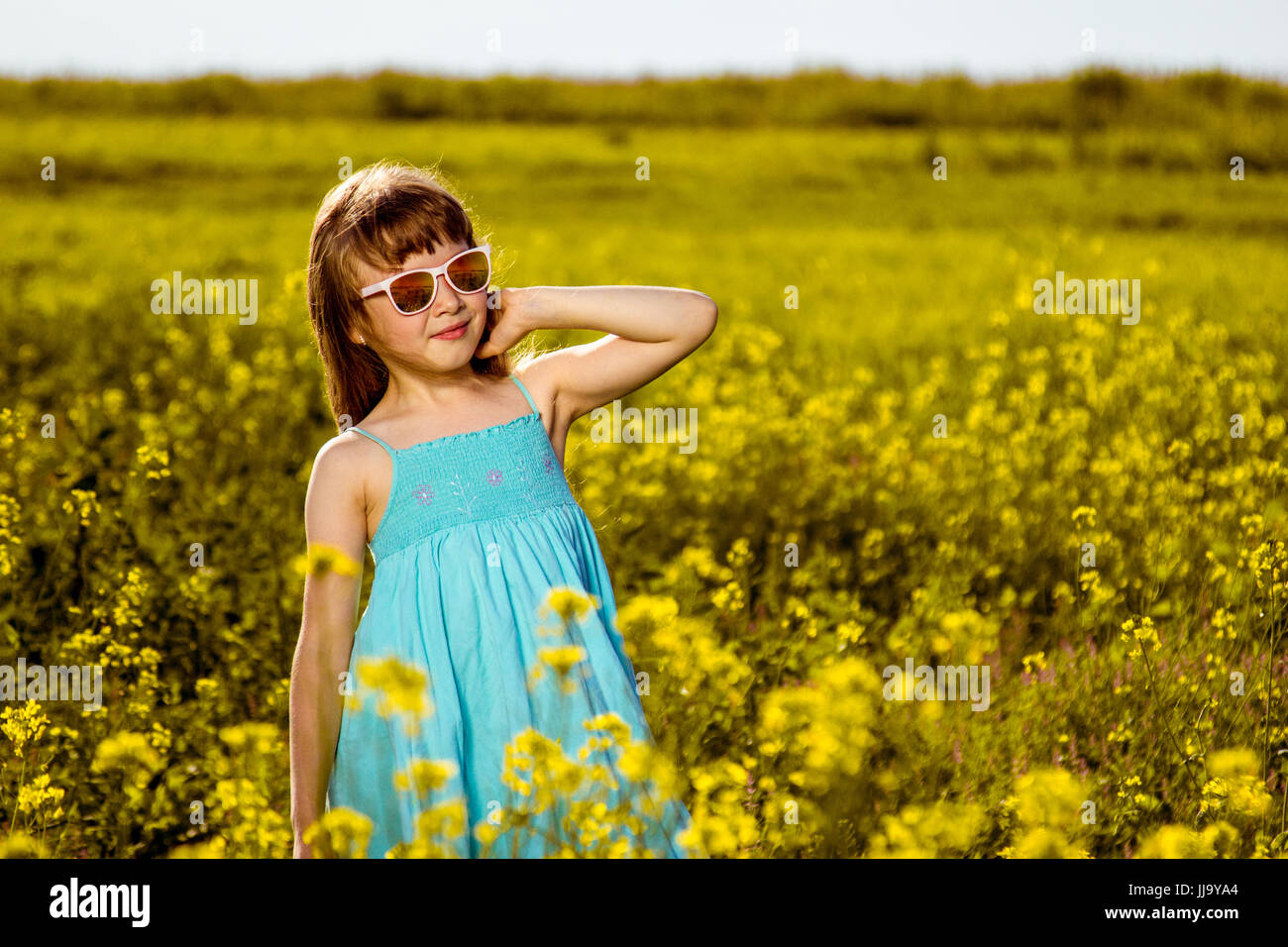 Ragazza in un abito blu in un campo. Fiori gialli in estate. Mattina di sole in natura. Foto Stock