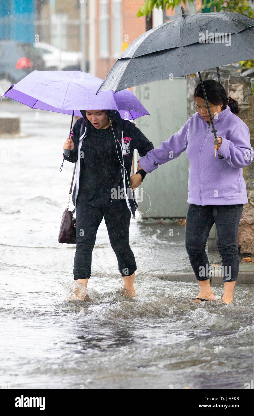 Due donna a piedi attraverso il flash l'acqua di allagamento sul loro modo home dopo forti piogge ha causato allagamenti per la A525 in estate durante il tuono e le tempeste di fulmini che ha colpito la zona, Rhyl, Galles del Nord, Regno Unito Foto Stock