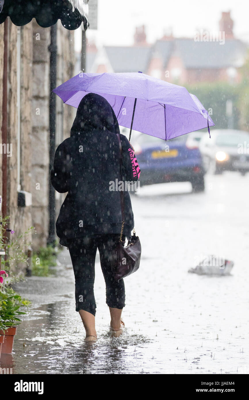 Una donna cammina attraverso allagamenti acqua sul suo modo home dopo forti piogge ha causato allagamenti per la A525 in estate durante il tuono e le tempeste di fulmini che ha colpito la zona, Rhyl, Galles del Nord, Regno Unito Foto Stock