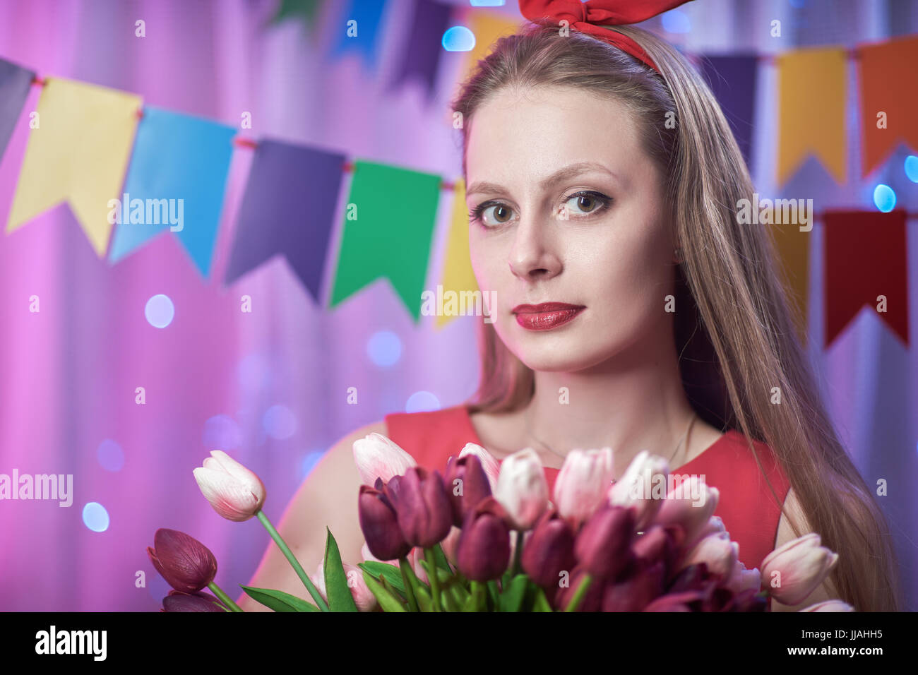 Il concetto: la celebrazione di compleanno. bella giovane vintage lo stile pin up girl in piedi in una colorata illumina la scena tenendo i fiori. Foto Stock