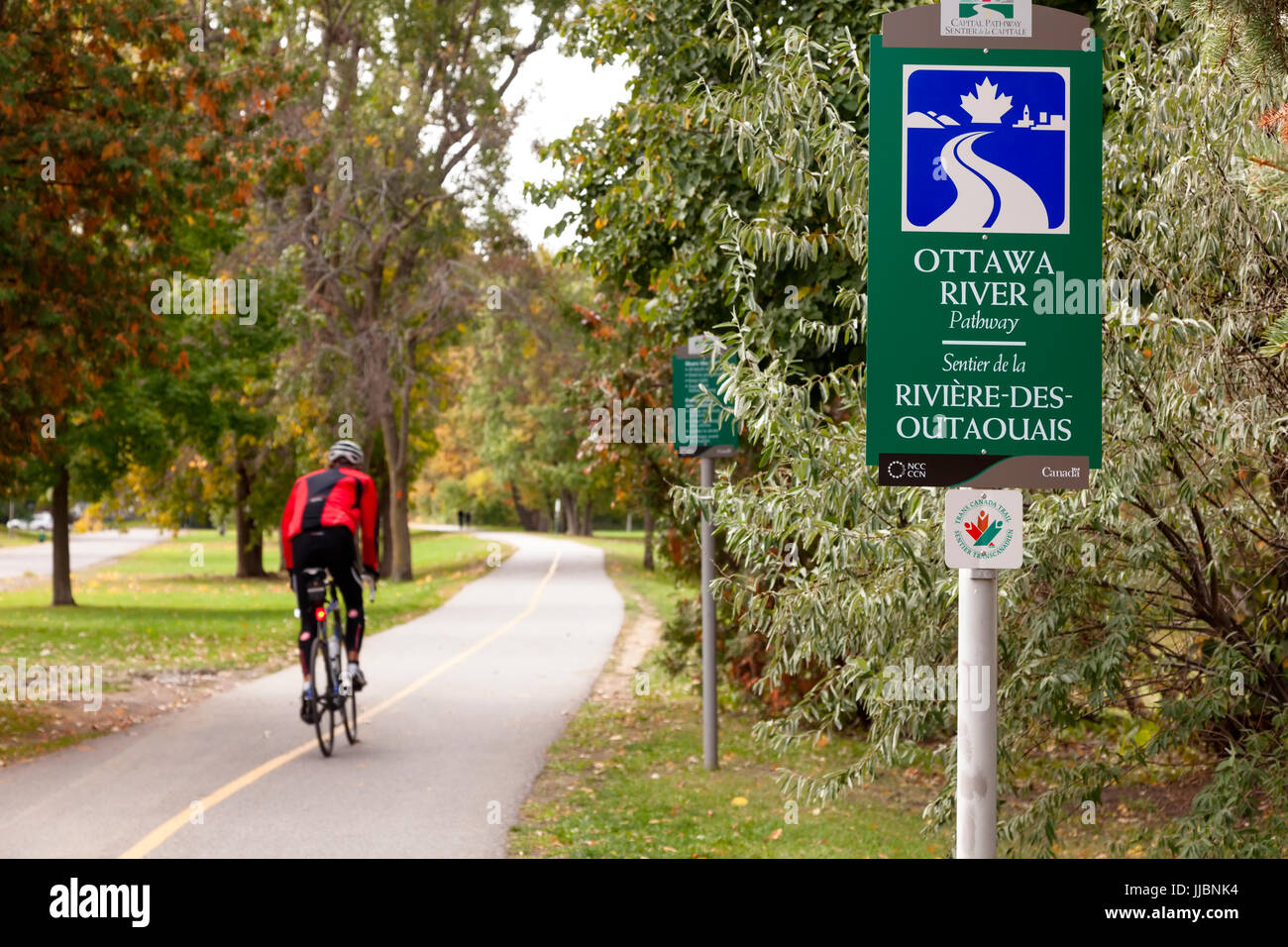 Un segno per il fiume Ottawa o percorso di percorso di capitale che è anche parte della Trans Canada Trail con un ciclista che passa da a Brittania Park. Foto Stock