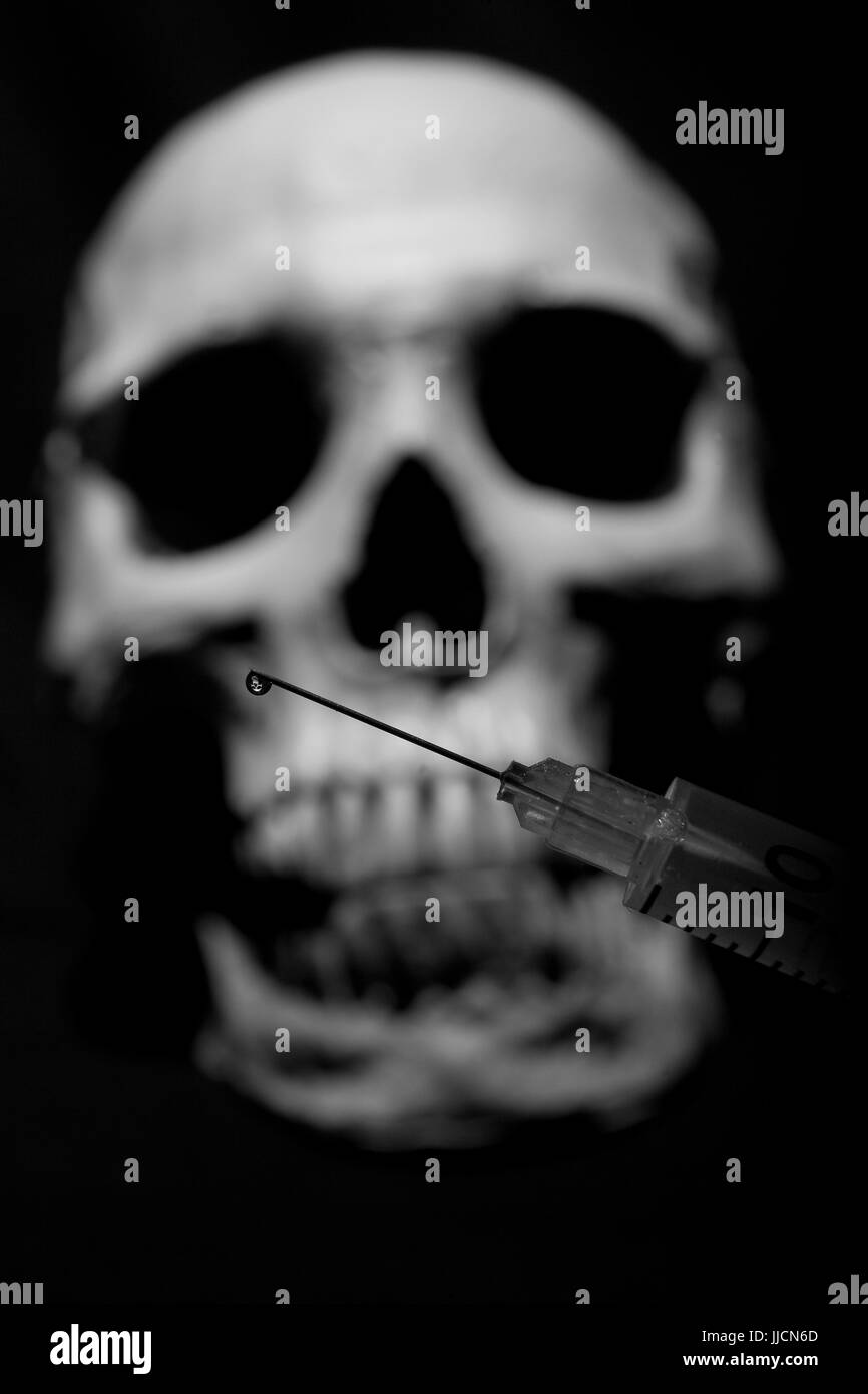 Una goccia di un farmaco sulla punta della siringa sullo sfondo di un teschio umano. Ancora in vita. Foto Stock
