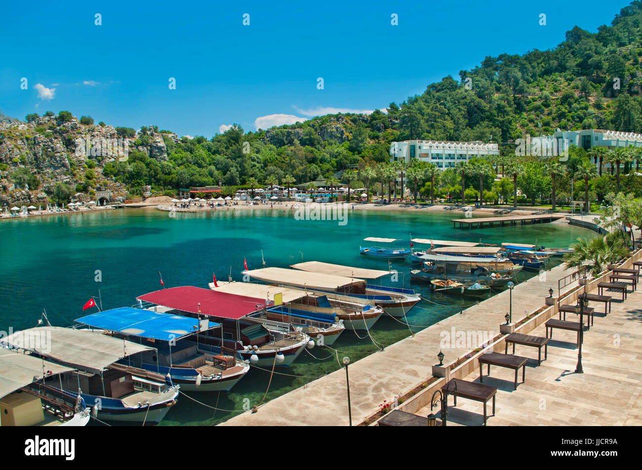 Piccoli taxi turistici barche ormeggiate in fila alla passeggiata lungomare con la spiaggia e gli hotel a sfondo nella piccola cittadina di turunc vicino a Marmaris, Turchia Foto Stock