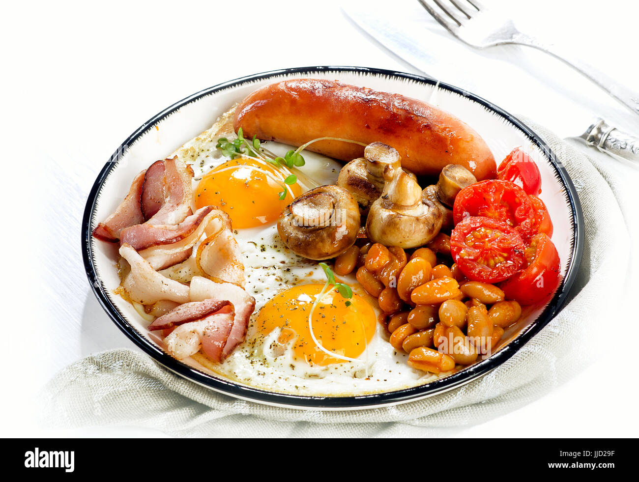 Prima colazione Inglese con uovo fritto, fagioli, pomodori, funghi, pancetta e salsicce su una piastra bianca Foto Stock