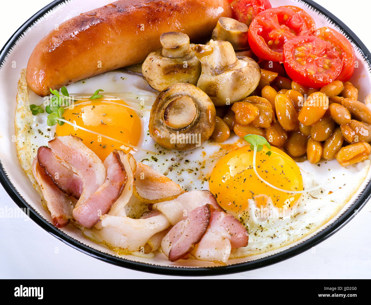 Prima colazione Inglese con uovo fritto, fagioli, pomodori, funghi e pancetta e salsiccia sulla piastra bianca Foto Stock