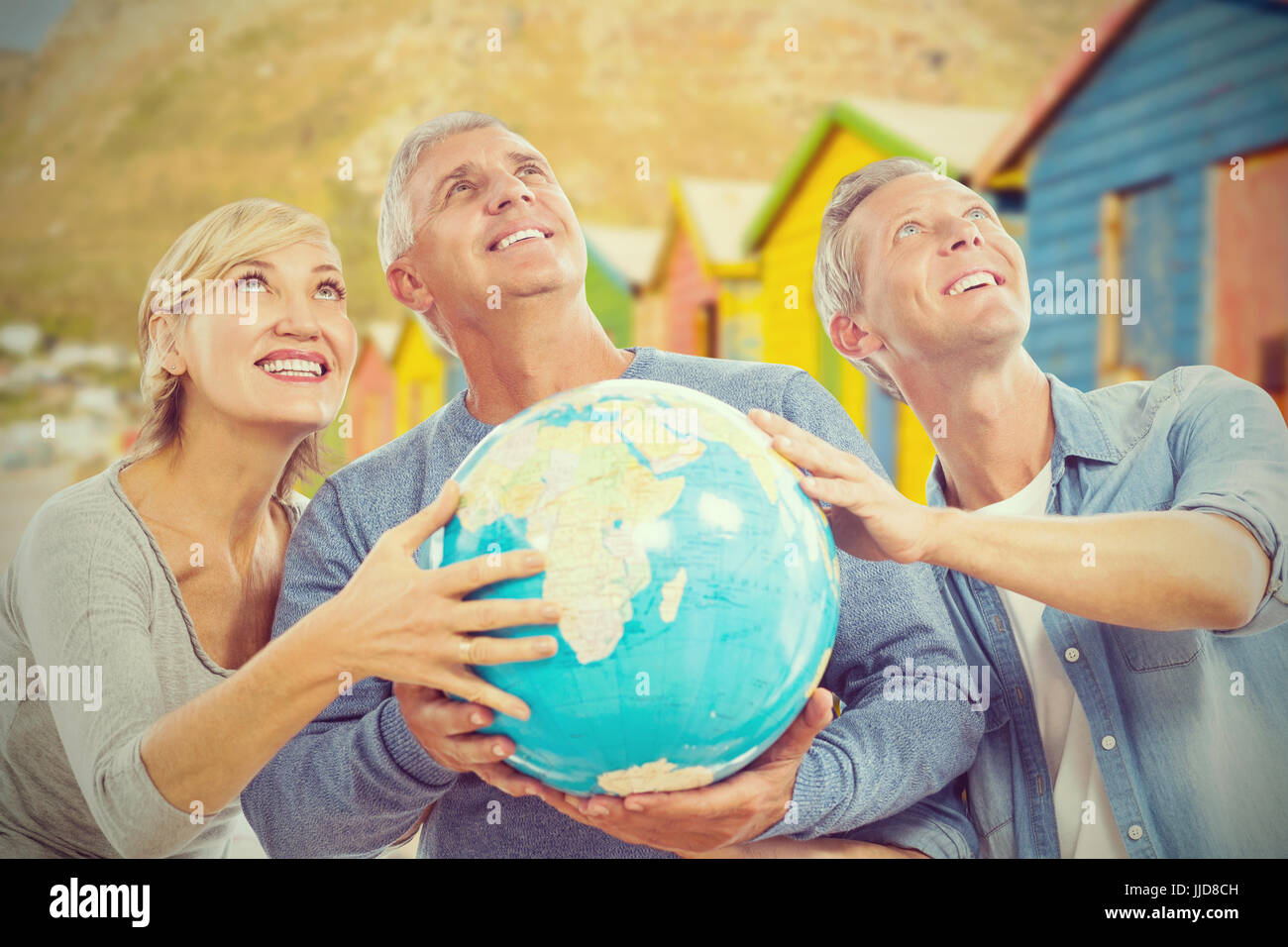 Popolo sorridente guardando verso l'alto tenendo premuto contro il globo multi colore capanne di spiaggia di sabbia Foto Stock