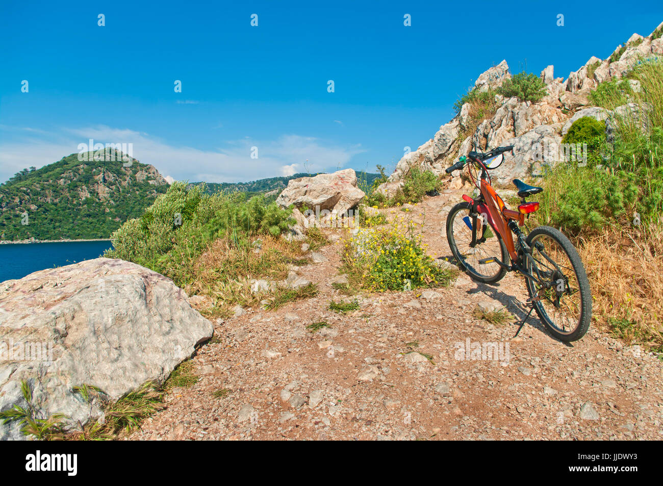 Orange mountain bike permanente al picco roccioso sovrastante il mare egeo a sunne giorno, Marmaris, Turchia Foto Stock