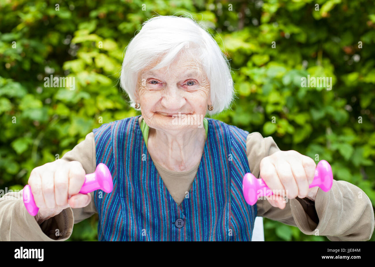 Foto di eccitato donna anziana facendo sport esercizi all'aperto nel giardino, azienda rosa manubri Foto Stock