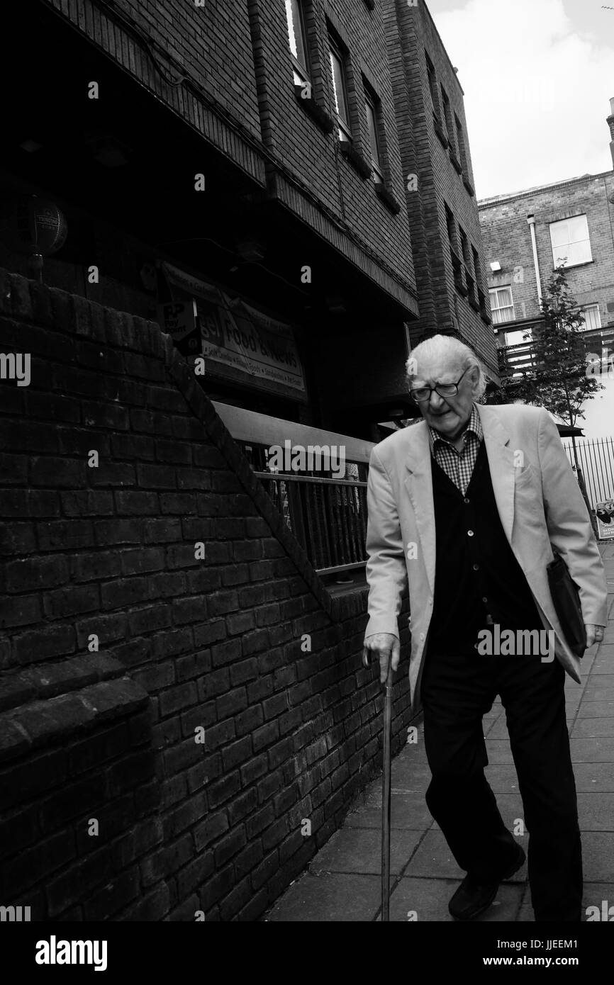 Uomo anziano con bastone cammina lentamente su una strada nel quartiere di Islington, Londra Foto Stock