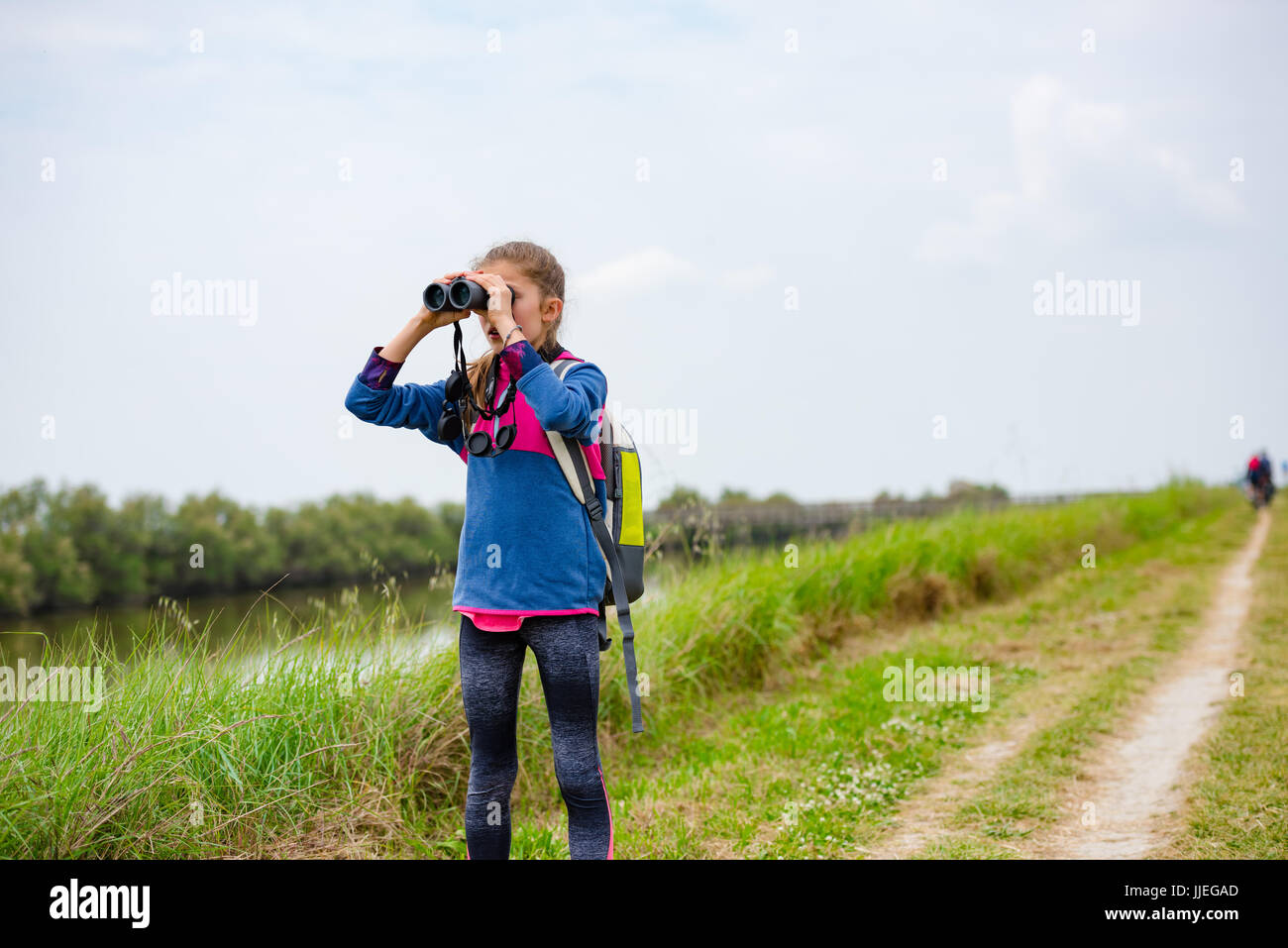 Ragazza giovane guardando attraverso il binocolo su un sentiero vicino al fiume Foto Stock